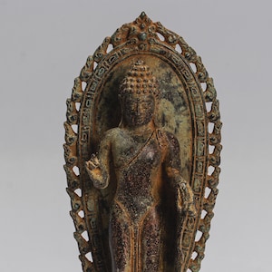 May include: A bronze statue of a Buddha standing on a base with a decorative halo. The statue is in a seated pose with the right hand raised in a gesture of blessing. The statue is weathered and has a green patina.
