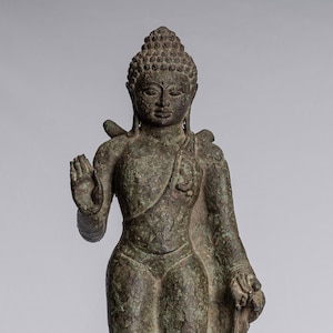May include: A bronze statue of a standing Buddha with a serene expression. The statue is on a wooden base and has a green patina.
