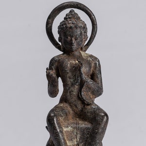 Könnte beinhalten: Eine dunkle Bronze-Statue eines sitzenden Buddha mit einem Heiligenschein. Der Buddha trägt eine Robe und hat einen ruhigen Ausdruck. Die Statue steht auf einem mehrstufigen Sockel.