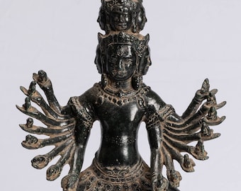 Può includere: Una scultura in bronzo nero di una divinità con più teste e più braccia, in piedi su una base di loto. La divinità ha un'espressione feroce ed è adornata con dettagli intricati.