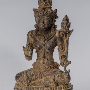 Könnte beinhalten: Eine Bronzestatue einer sitzenden weiblichen Gottheit, die eine Lotusblume in der Hand hält. Sie trägt eine Krone und aufwendigen Schmuck. Die Statue befindet sich in einer meditativen Pose und hat einen ruhigen Ausdruck.