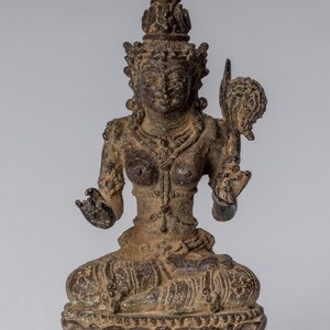 Puede incluir: Una estatua de bronce de una deidad sentada con una corona y joyas elaboradas. La deidad sostiene una flor de loto en una mano y tiene una expresión serena.