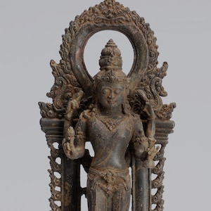 May include: A bronze statue of a deity standing on a pedestal with intricate carvings. The deity is adorned with jewellery and has a serene expression. The statue is surrounded by a decorative frame.