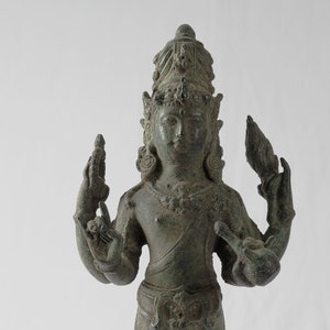 May include: A bronze statue of a deity standing on a square base. The deity has four arms, a crown, and is wearing a long robe. The statue is green and has a weathered patina.