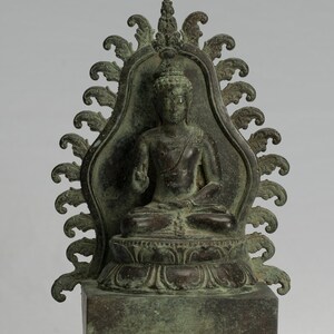 May include: A bronze statue of a seated Buddha, with a decorative halo and a lotus throne. The statue has a green patina and is in a meditative pose.