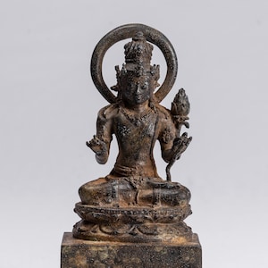 Può includere: Una statua di bronzo di un Buddha seduto con un'aureola e un fiore di loto in mano. La statua è su una base a più livelli.