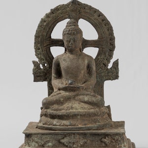 May include: A bronze statue of a seated Buddha, with a wheel of dharma behind the figure. The statue is on a square base with intricate carvings.