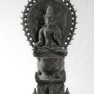 May include: A green bronze statue of a seated Buddha figure with a halo and intricate details. The Buddha is seated on a lotus throne with a base that features additional decorative elements.