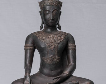 Op de afbeelding: Een donker bronzen beeld van een zittende Boeddha met een puntige kroon en ingewikkelde details. De Boeddha zit in een meditatieve houding met handen die op de schoot rusten. Het beeld staat op een vierkante basis met decoratieve gravures.