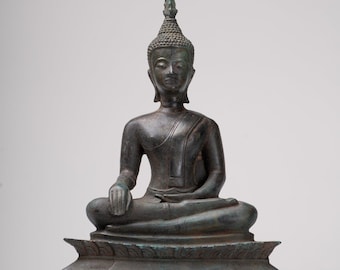 May include: A dark bronze statue of a seated Buddha with a pointed crown, wearing a robe and sitting on a tiered base.
