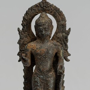 Op de afbeelding: Een bronzen beeld van een staande Boeddha met een halo en een decoratieve basis. Het beeld is verweerd en heeft een donkerbruine patina.