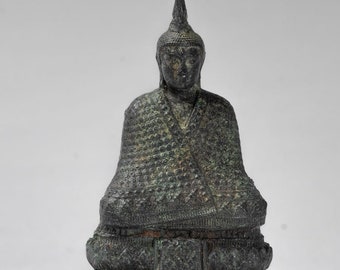 May include: A small, dark green bronze statue of a seated Buddha with a pointed crown. The Buddha is wearing a robe with a patterned design and is seated on a lotus throne.