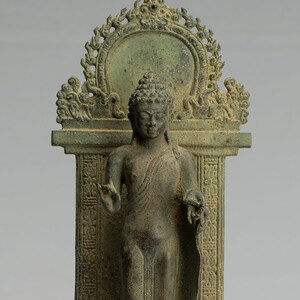 May include: A bronze statue of a standing Buddha, with a serene expression, wearing a robe and standing on a lotus base. The statue is set within a decorative archway with intricate details.