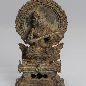 Può includere: Una statua di bronzo di una divinità seduta su un trono con un'aureola dietro la testa. La divinità tiene una spada nella mano destra e un serpente nella mano sinistra. La statua è su una base quadrata con dettagli intricati.