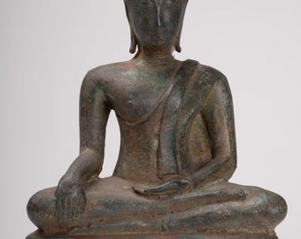 May include: Bronze Buddha statue in a seated meditation pose. The figure has a serene expression, draped in a robe, and sits atop a square base. The statue has a weathered, aged appearance with hints of green patina.