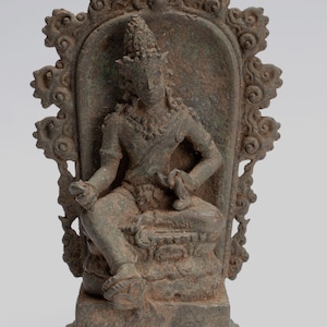 May include: A bronze sculpture of a seated deity with a crown and elaborate headdress. The deity is seated on a throne with a decorative back and a base. The sculpture is in a dark brown colour with green patina.