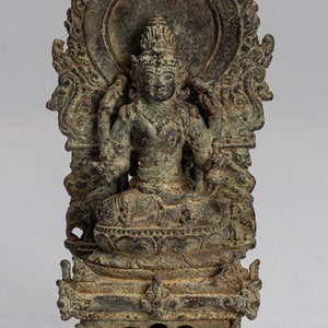 May include: A bronze statue of a seated deity with a halo and elaborate ornamentation. The statue is in a seated position with hands in a mudra gesture. The deity is wearing a crown and jewelry. The statue is on a base with a square platform.