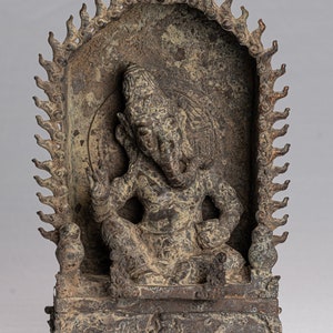 May include: A bronze sculpture of the Hindu deity Ganesha, depicted seated in a meditative pose with his trunk raised. The sculpture is housed within a decorative frame with a flame-like border.