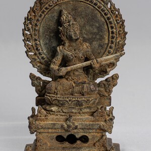 Könnte beinhalten: Eine Bronzestatue einer sitzenden Gottheit mit einem Heiligenschein und einem Musikinstrument. Die Statue sitzt mit einem Heiligenschein hinter dem Kopf und einem Musikinstrument in den Händen. Die Statue ist aus Bronze und hat eine dunkelbraune Patina.