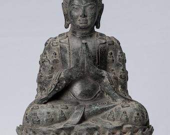 May include: A bronze statue of a seated Buddha with hands in prayer position. The Buddha is wearing a robe and is seated on a lotus throne. The statue is in a dark green patina.