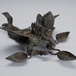 May include: A bronze sculpture of a mythical creature with wings and a bird-like head. The creature is holding three small bowls in its hands. The sculpture is in a reclining position.