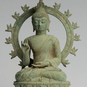 Puede incluir: Una estatua de bronce verde de un Buda sentado con un halo y un pequeño paraguas sobre su cabeza. La estatua está en una postura meditativa con una mano levantada en un gesto de bendición.