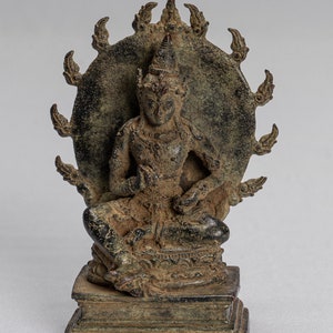 Può includere: Statua in bronzo di una figura seduta con un'aureola. La figura è adornata con una corona e gioielli ed è seduta su una base dettagliata. L'aureola presenta una serie di proiezioni a forma di fiamma. La statua ha un aspetto antico e usurato.