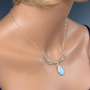 May include: A silver necklace with a delicate filigree design and a teardrop-shaped blue gemstone pendant.