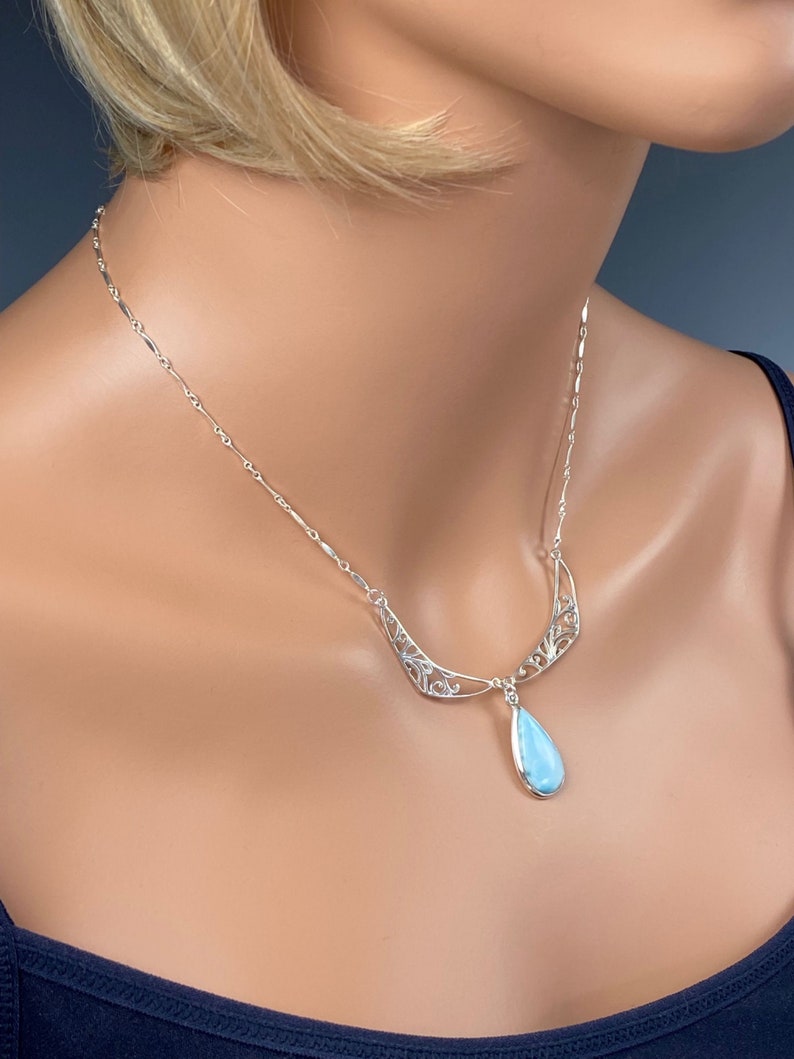 May include: A silver necklace with a delicate filigree design and a teardrop-shaped blue gemstone pendant.