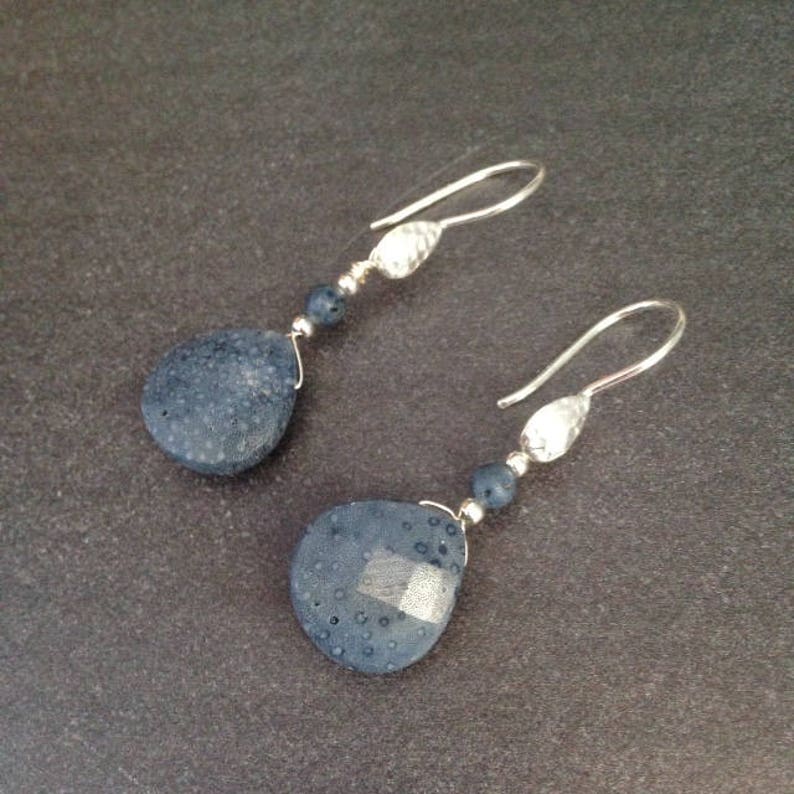 May include: A pair of silver dangle earrings with dark blue teardrop-shaped stones. The stones have a textured surface.