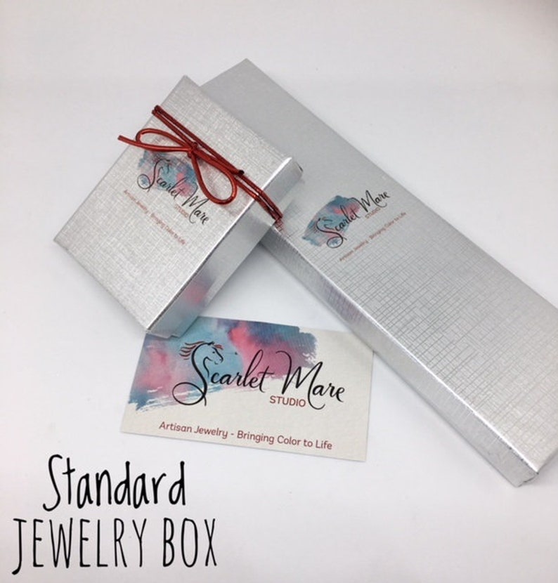 May include: A silver jewelry box with a red ribbon and the text "Scarlet Mare Studio" printed on the box. The text "Artisan Jewelry - Bringing Color to Life" is also printed on the box. The box is labeled "Standard Jewelry Box".