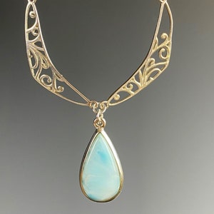 May include: A silver necklace with a delicate filigree design and a teardrop-shaped blue gemstone pendant.