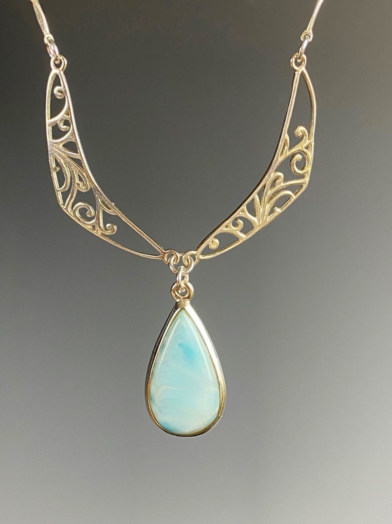 May include: A silver necklace with a delicate filigree design and a teardrop-shaped blue gemstone pendant.