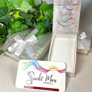 May include: A silver gift box with a white satin ribbon and a white card with the text "Scarlet Mare Studio" and "Artisan Jewelry - Bringing Color to Life".