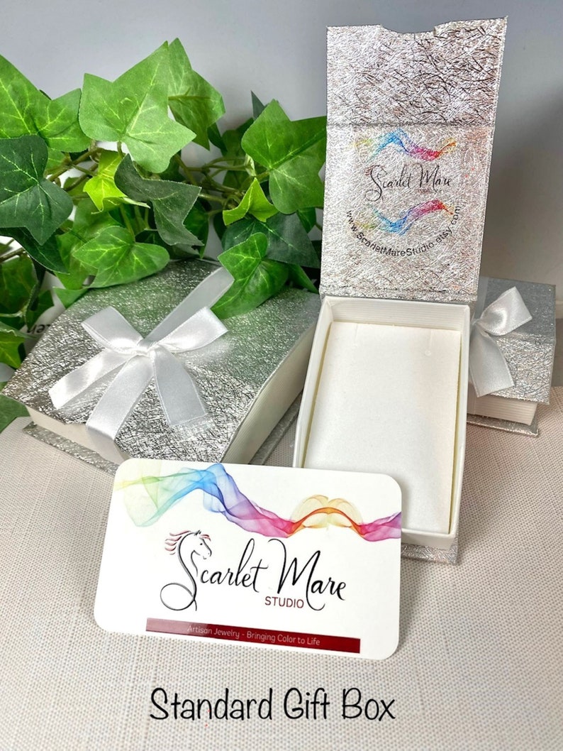 May include: A silver gift box with a white satin ribbon and a white card with the text "Scarlet Mare Studio" and "Artisan Jewelry - Bringing Color to Life".