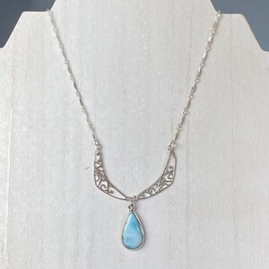 May include: A silver necklace with a teardrop-shaped blue gemstone pendant. The necklace features a delicate, filigree design.