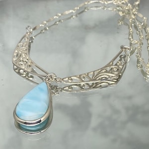 May include: A silver filigree necklace with a teardrop-shaped blue gemstone pendant.