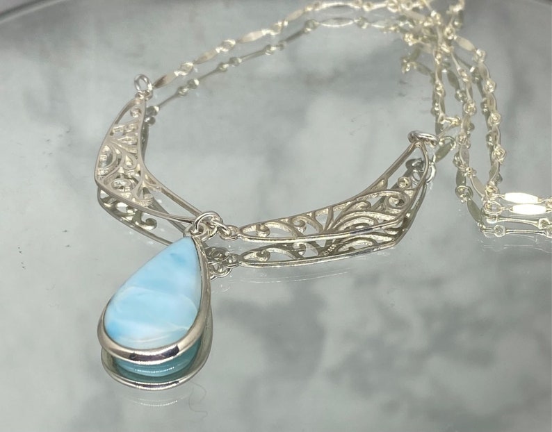 May include: A silver filigree necklace with a teardrop-shaped blue gemstone pendant.