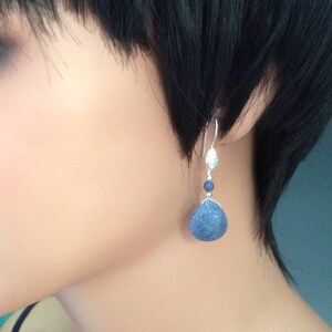 May include: Silver dangle earrings with a blue teardrop-shaped stone and a smaller blue bead.