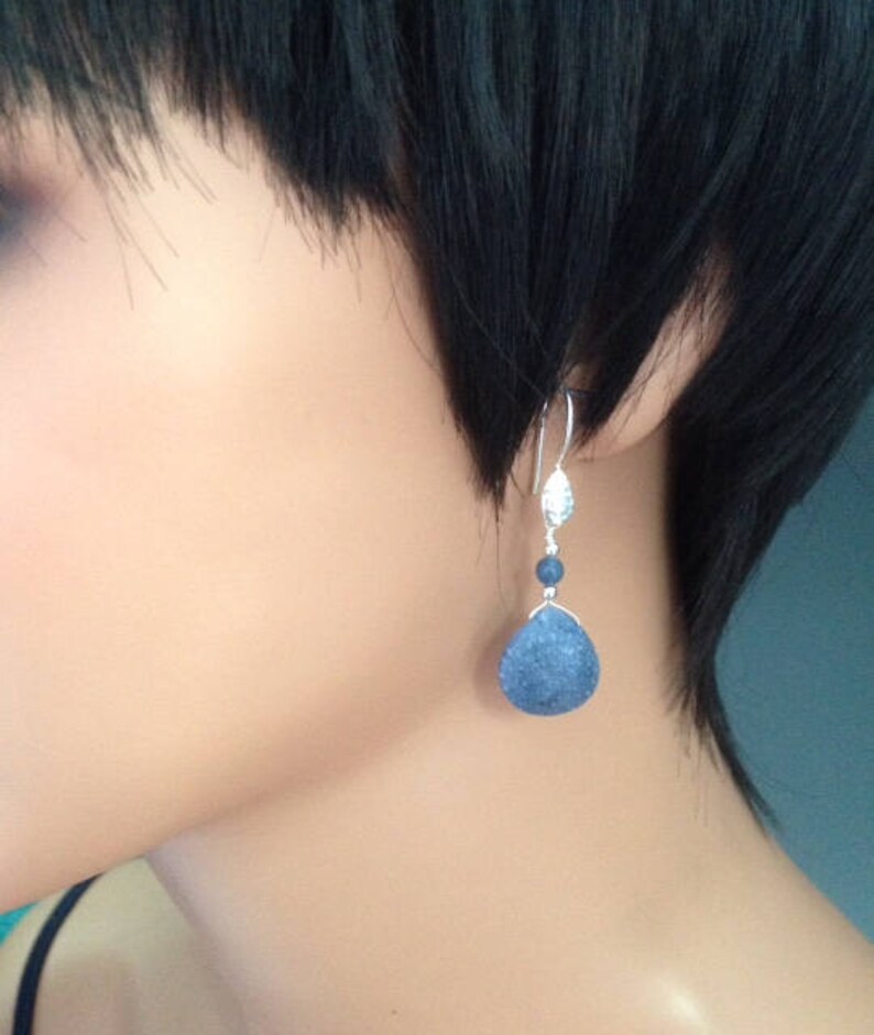 May include: Silver dangle earrings with a blue teardrop-shaped stone and a smaller blue bead.