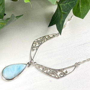 May include: A silver filigree necklace with a teardrop-shaped blue opal pendant.