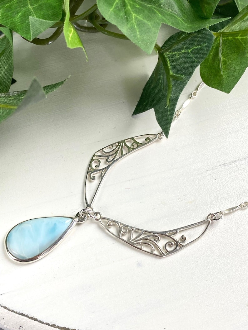 May include: A silver filigree necklace with a teardrop-shaped blue opal pendant.