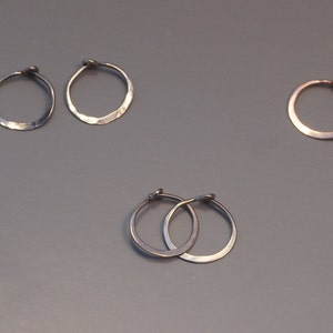 May include: Five pairs of silver and gold hoop earrings. The earrings are all different sizes and have a hammered texture.