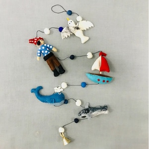 May include: A felt nautical mobile with a blue whale, a shark, a sailboat, a seagull, and a pirate. The mobile is strung with white and blue beads and has a gold bell at the bottom.
