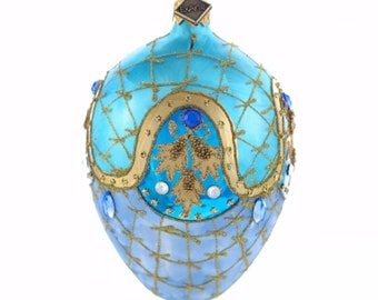May include: A teardrop-shaped glass ornament in shades of light and bright blue, featuring a gold glitter lattice pattern, gold painted arches, gold leaf-like accents, and embedded blue and clear rhinestones with an ExArte brand tag.