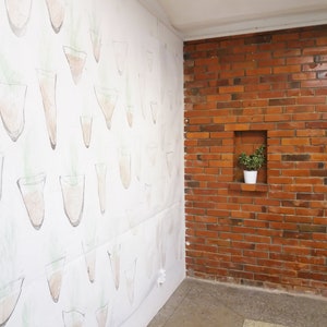May include: A white wall with a repeating pattern of hand-drawn potted plants. The wall is next to a brick wall with a small potted plant in a niche.