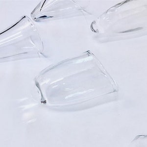 May include: A set of five clear glass cups with a rounded shape. The cups are arranged on a white surface.