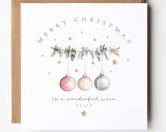 May include: A square Christmas card with a brown envelope. The card features the words "MERRY CHRISTMAS" above a garland with three hanging ornaments in pink, white, and green. The text "to a wonderful niece ELLIE" is below.