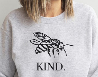 May include: A gray sweatshirt with a black bee illustration and the word "KIND." printed on the front.