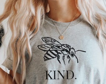Może przedstawiać: Szary t-shirt z czarnym nadrukiem pszczoły i napisem "KIND." poniżej.